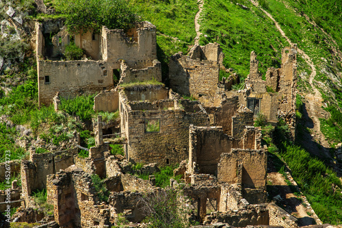 Abandoned houses of the ancient village of Gamsutl with destroyed stone walls of the building on the top of a mountain peak against the background of mountains in summer in Dagestan, Russia photo