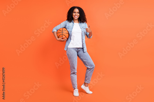 Full body photo of funny millennial brunette lady hold ball wear jeans shirt shoes isolated on orange background © deagreez