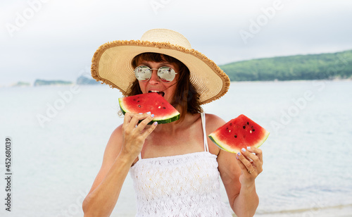 Portrait elegant tanned woman in straw hat eating fresh appetizing watermelon slice on beach
