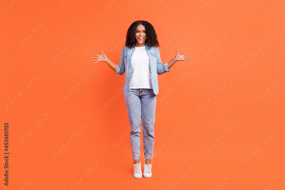 Full length photo of impressed millennial brunette lady wear shirt jeans sneakers isolated on orange color background Full length photo of impressed millennial brunette lady wear shirt jeans sneakers isolated on orange color background