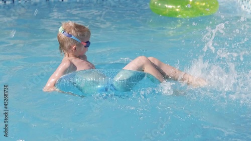 Little boy in swimming pool, child having fun, sitting on blue swimming ring, playing under water. Summer travel family hotel vacation tourists photo