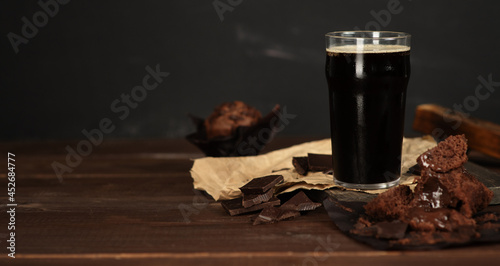 Photo Glass of beer stout standing on wooden board next to chocolate muffin