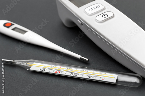 Different type of thermometers on grey background. Infrared, electronic and mercury thermometers. photo