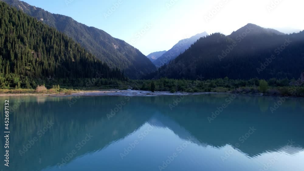 View of the mountain lake Issyk from a height. Turquoise-emerald water from the glacier. Reflection of mountains, forests and the sun on the water. The river flows into the lake. Issyk Dam. Kazakhstan View of the mountain lake Issyk from a height. Turquoise-emerald water from the glacier. Reflection of mountains, forests and the sun on the water. The river flows into the lake. Issyk Dam. Kazakhstan