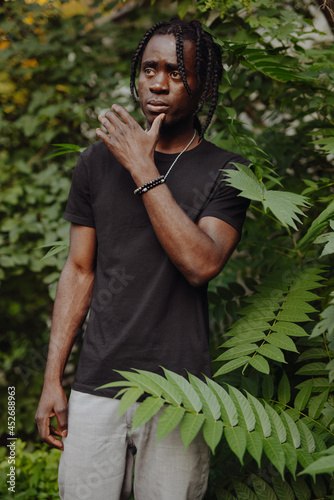 Portrait African man in black t-shirt with dreadlocks in green leaves