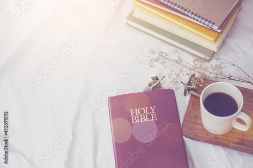 The Holy Bible  and a cup of black coffee over blurred book stack on the bed, Christian background morning devotional concept with copy space photo