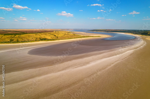 Amazing beauty of dried salty lake of light beige color surrounded by green and yellow fields. Aerial view of a bright salt reservoir in summer. Shot. Top view of a bird's-eye view on drying estuary