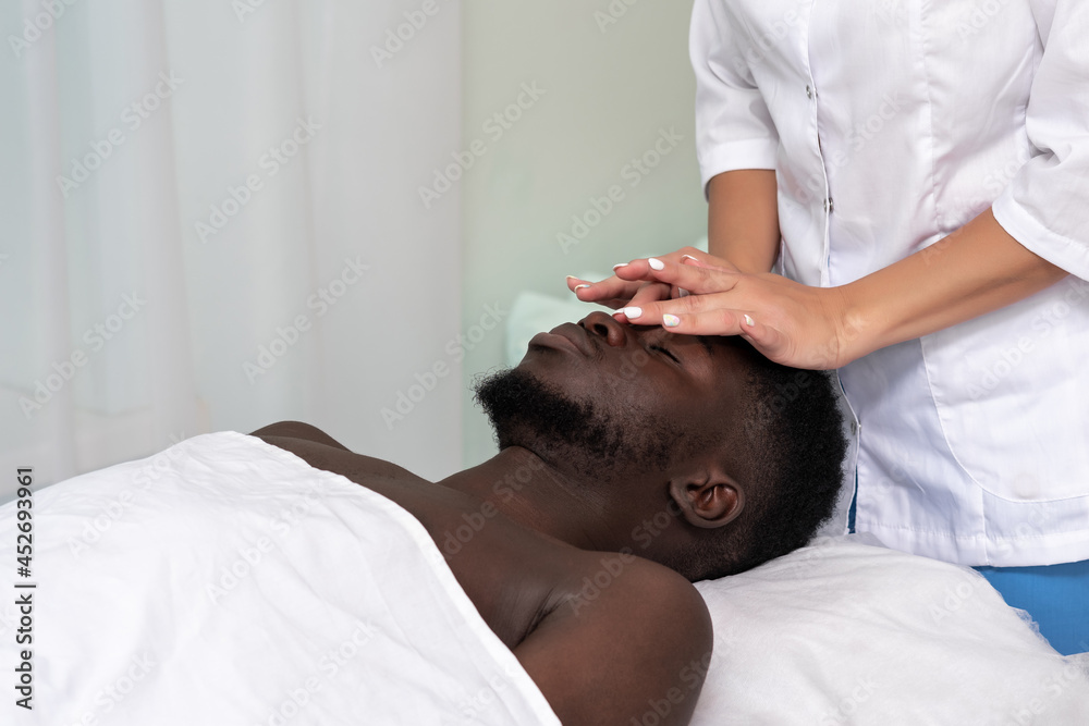 Fototapeta premium woman masseur doing a face and head massage to black man