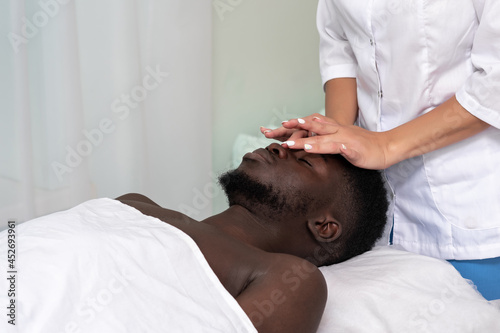 woman masseur doing a face and head massage to black man