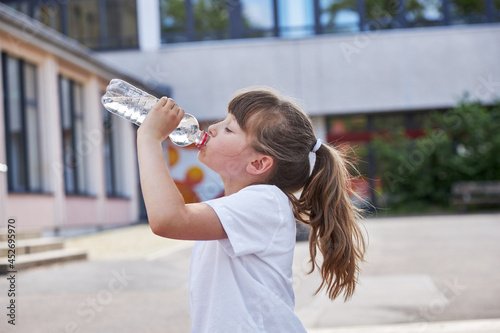 Bild auf Leinwand Schoolgirl girl drinks fresh mineral water from a bottle in the schoolyard
