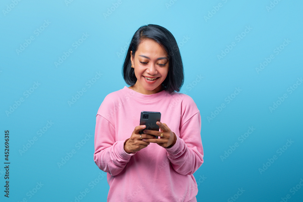 Beautiful Asian woman smiling looking to smartphone isolated on blue background Beautiful Asian woman smiling looking to smartphone isolated on blue background