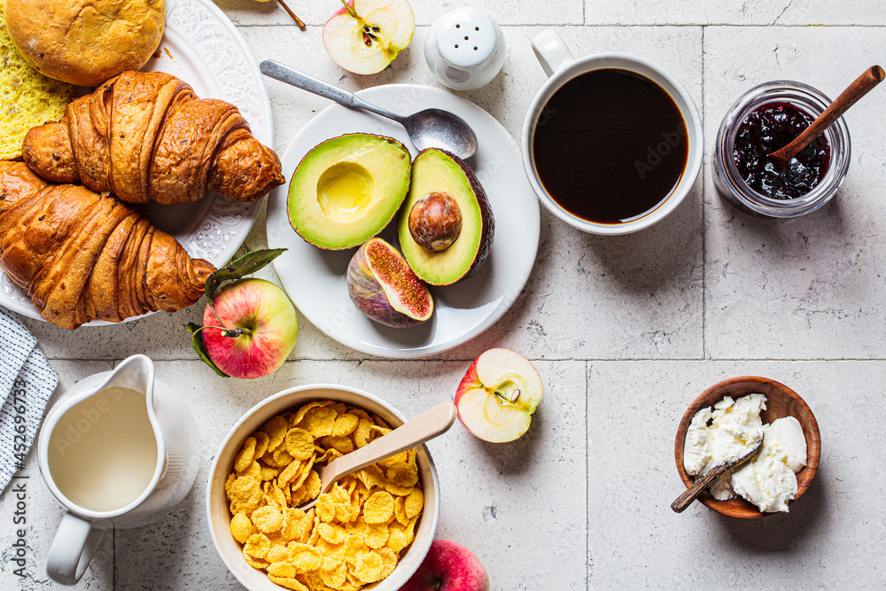 Breakfast table with cornflakes, croissants, fruit, cheese and cup of coffee. Gray tile background, top view.