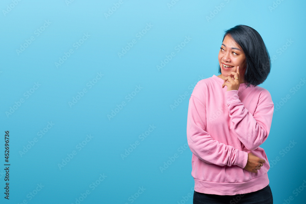 Attractive asian woman with smiling expression and looking at empty space on blue background Attractive asian woman with smiling expression and looking at empty space on blue background