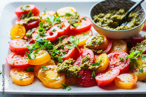 Red and yellow tomatoes salad with pesto sauce on gray plate. Italian cuisine concept.