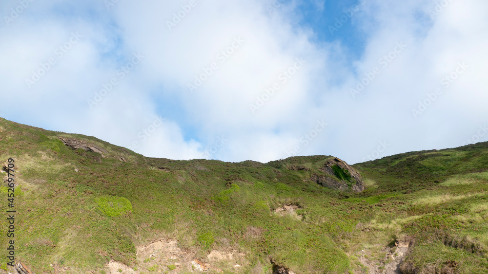 Ladera de hierba verde y ceilo azul con nubes blancas