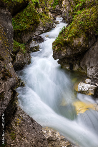 Fototapeta Naklejka Na Ścianę i Meble -  A stream of water is flowing into an alpine gorge surrounded by green vegetation