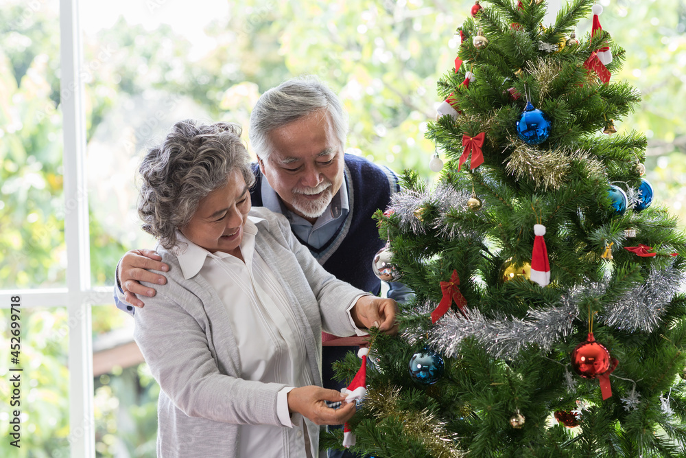 Happy Asian senior couple decorating Christmas tree together at home. Senior couple spending time together on Christmas day while prepare gift or decorate Christmas tree in living room at home Happy Asian senior couple decorating Christmas tree together at home. Senior couple spending time together on Christmas day while prepare gift or decorate Christmas tree in living room at home