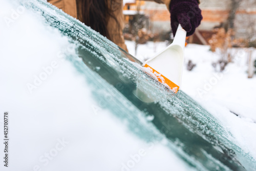 Woman cleans snow from her car with a scraper