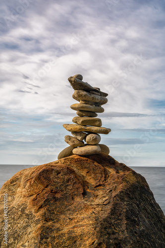 meditative rock cairn on top of a boulder with long exposure ocean and sky in the background