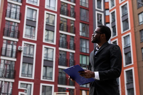 man contractor with floor plan in hands looking on building at c