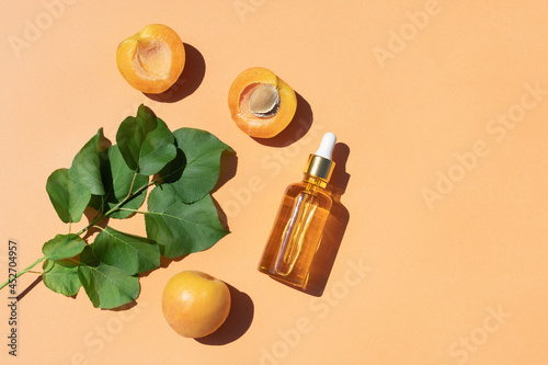 Serum or oil in glass bottle with fresh apricots fruit on pastel orange background. Natural cosmetic beauty product branding mock-up for brightening cream, body lotion, facial foam. Flat lay.