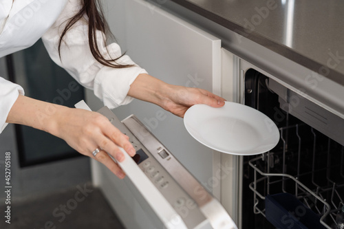Woman using modern built-in dishwasher machine in kitchen