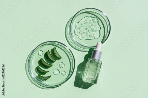 Flat lay of cosmetics serum and and laboratory glassware with fresh leaves of aloe vera on bright green background. Organic cosmetics. Top view flat lay, copy space. Cosmetics, SPA branding, mock-up.