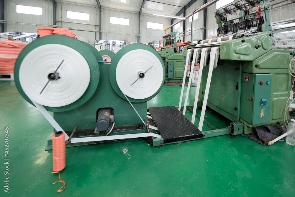 Machinery and forklift are in operation in the bag weaving workshop of a packaging factory Machinery and forklift are in operation in the bag weaving workshop of a packaging factory
