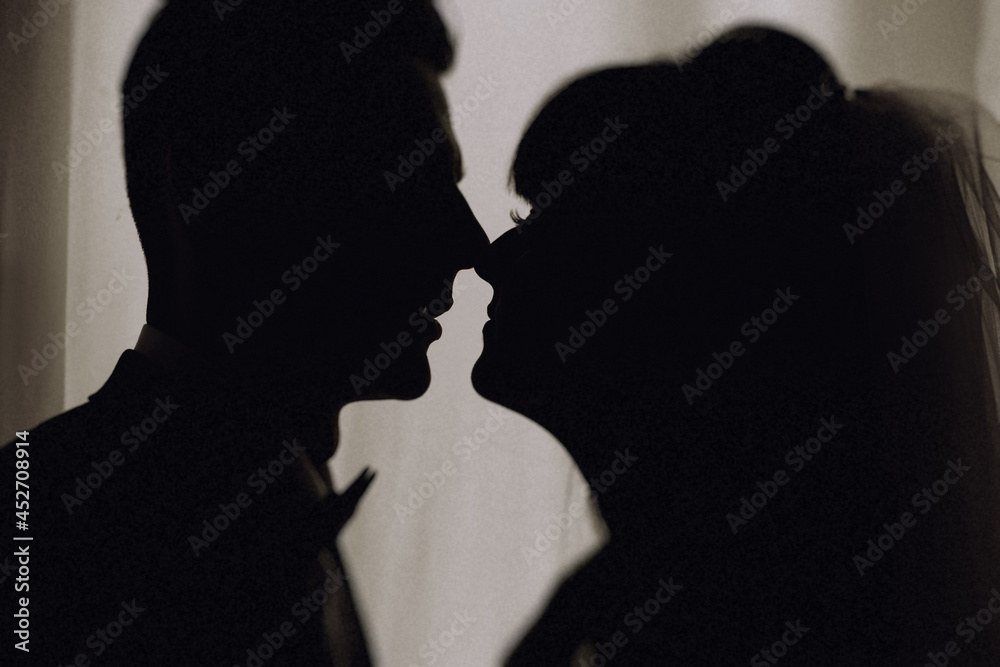 Side view of silhouettes of interracial couple in love looking at each other. Silhouette Of The Bride and Groom Standing At The Window Of Their Wedding Day. Side view of silhouettes of interracial couple in love looking at each other. Silhouette Of The Bride and Groom Standing At The Window Of Their Wedding Day.