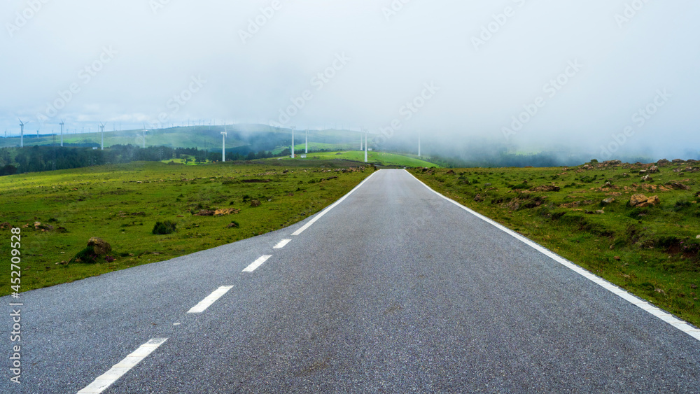 Carretera de montaña solitaria con un grupo de aerogeneradores eolicos entre la niebla Carretera de montaña solitaria con un grupo de aerogeneradores eolicos entre la niebla