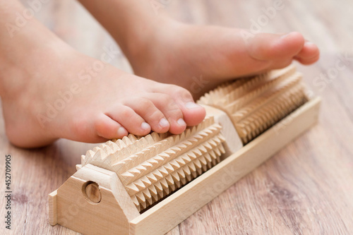 The girl does self-massage of the feet on a special wooden needle massager for the prevention of flat feet, valgus. Relaxation of the legs. photo