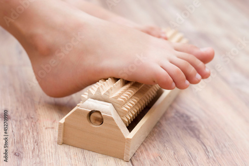 The girl does self-massage of the feet on a special wooden needle massager for the prevention of flat feet, valgus. Relaxation of the legs. photo