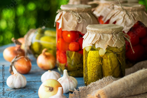 Pickled tomatoes and cucumbers in glass jars on an old wooden table. Summer harvest.