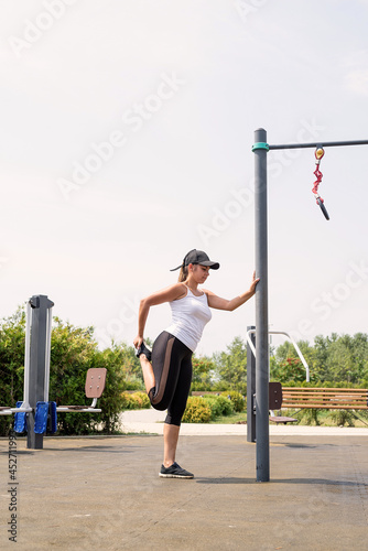Happy woman working out on the sports ground in sunny summer day stretching her legs