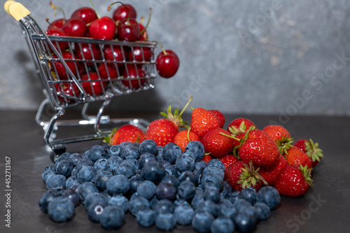 in a small shopping cart cherries, blueberries and strawberries on a dark background