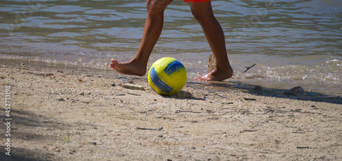 Jovem rapaz à jogar bola numa praia fluvial perto da água - juvenil photo