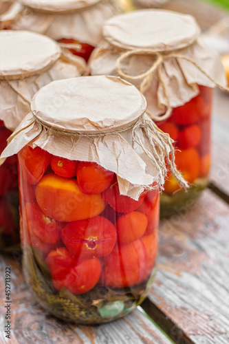 Pickled tomatoes in a glass jars on an old wooden table. Summer harvest.