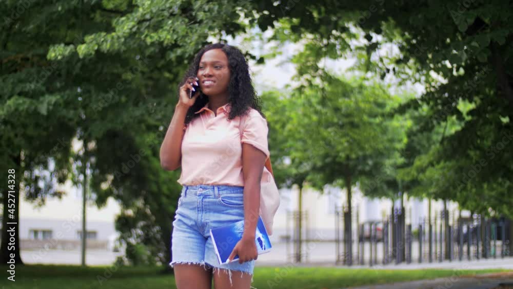 technology, education and people concept - happy smiling african american student girl with textbook calling on smartphone in city technology, education and people concept - happy smiling african american student girl with textbook calling on smartphone in city