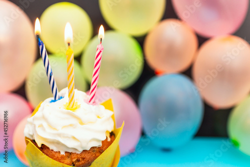Birthday cupcake.Pastel yellow birthday cupcake with candle and blurred balloons.colorful birthday.Closeup,copy space.