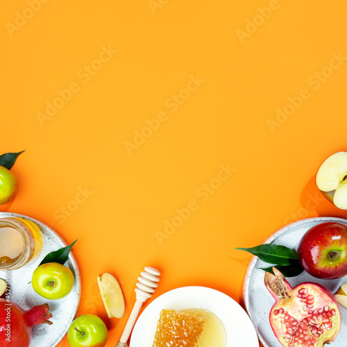 Honey, apple and pomegranate on a orange background. Concept Jewish New Year Happy holiday Rosh Hashanah. Creative layout of traditional symbols. View from above. Flat lay. Copy space. Shana Tova.
