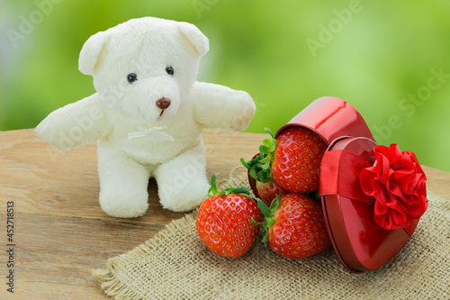 Strawerry in red heart shape box with little white bear doll on wooden table, Concept valentine's day photo
