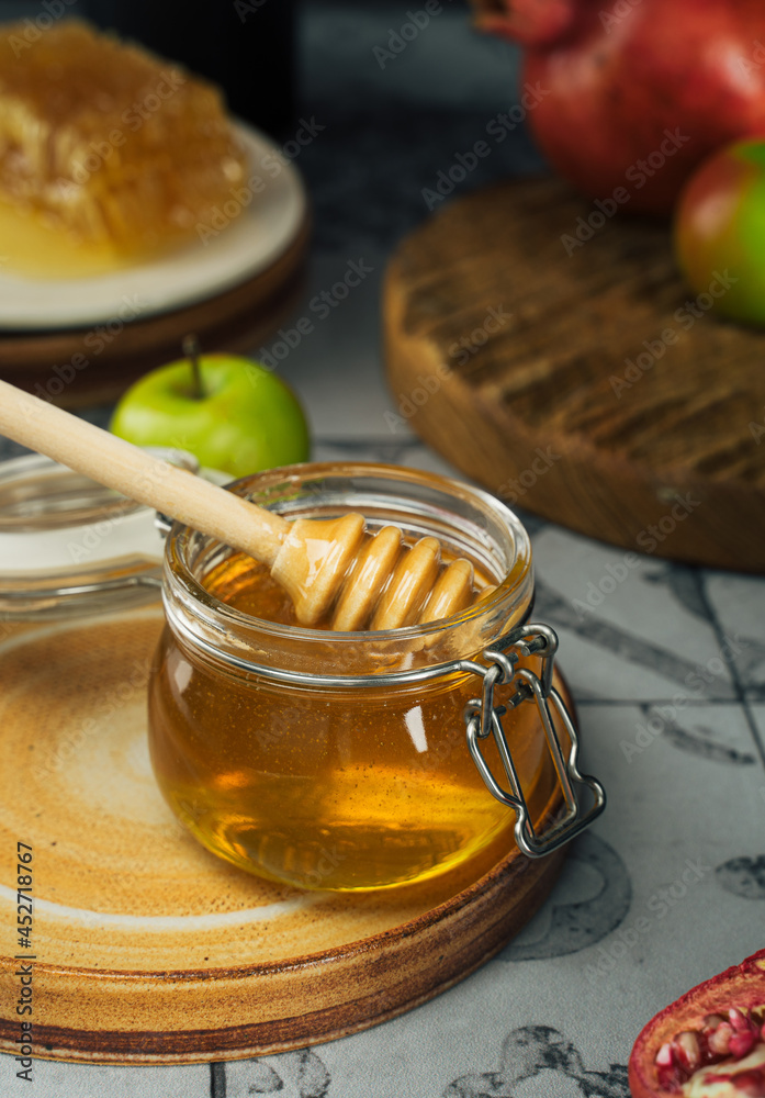 Glass jar with fresh honey, honey spoon, apple and pomegranate. Concept Jewish New Year Happy holiday Rosh Hashanah. layout of traditional symbols. View from above. Shana Tova Glass jar with fresh honey, honey spoon, apple and pomegranate. Concept Jewish New Year Happy holiday Rosh Hashanah. layout of traditional symbols. View from above. Shana Tova
