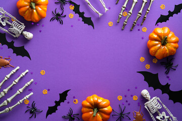 Halloween decorations on violet background. Flat lay pumpkins, bats, spiders, skeletons and confetti. Top view with copy space. Halloween concept.