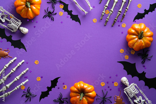 Halloween decorations on violet background. Flat lay pumpkins, bats, spiders, skeletons and confetti. Top view with copy space. Halloween concept.