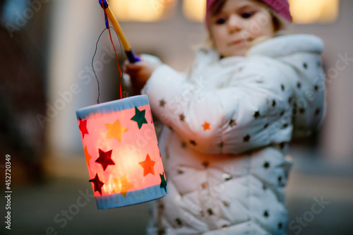 Close-up of little kid girl holding selfmade lanterns with candle for St. Martin procession. Healthy toddler child happy about children and family parade in kindergarten. German tradition Martinsumzug photo