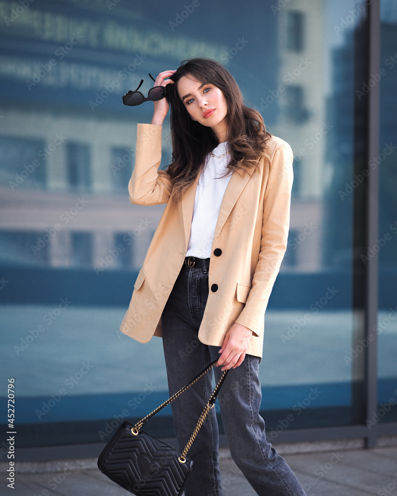 A woman stands on the background of a glass building in a jacket