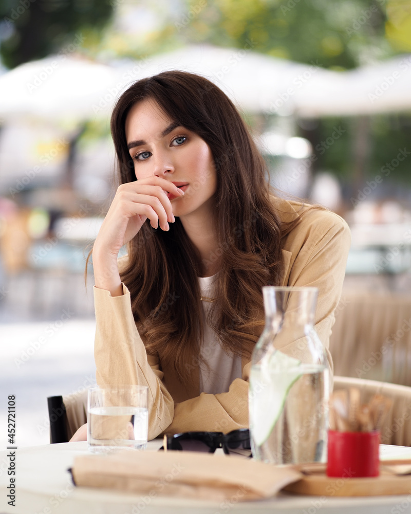 A woman on a summer terrace sits at a table in a beige jacket A woman on a summer terrace sits at a table in a beige jacket