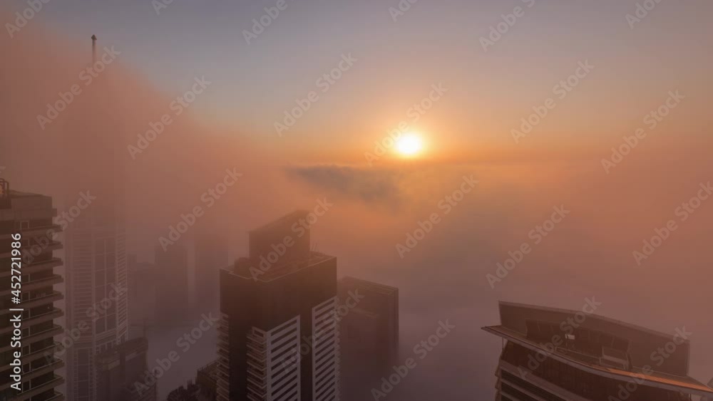 Rare early morning winter fog above the Dubai Marina skyline and skyscrapers lighted by sun aerial timelapse.