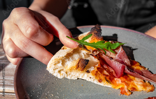 woman Hand takes a slice of meat neapolitan Pizza with Mozzarella cheese, ham, bacon, tomato, Spices on plate in cafe outdoor