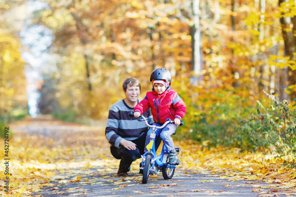 Little kid boy and his father in autumn park with a bicycle. Dad teaching his son biking Little kid boy and his father in autumn park with a bicycle. Dad teaching his son biking